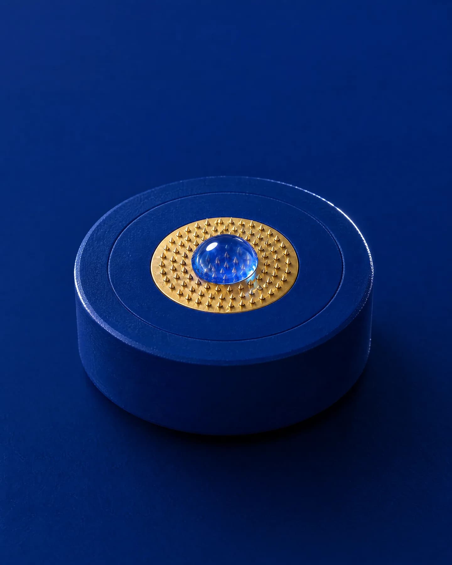 A bead of blue serum resting on the gold micro-needle pad of a single-use head.