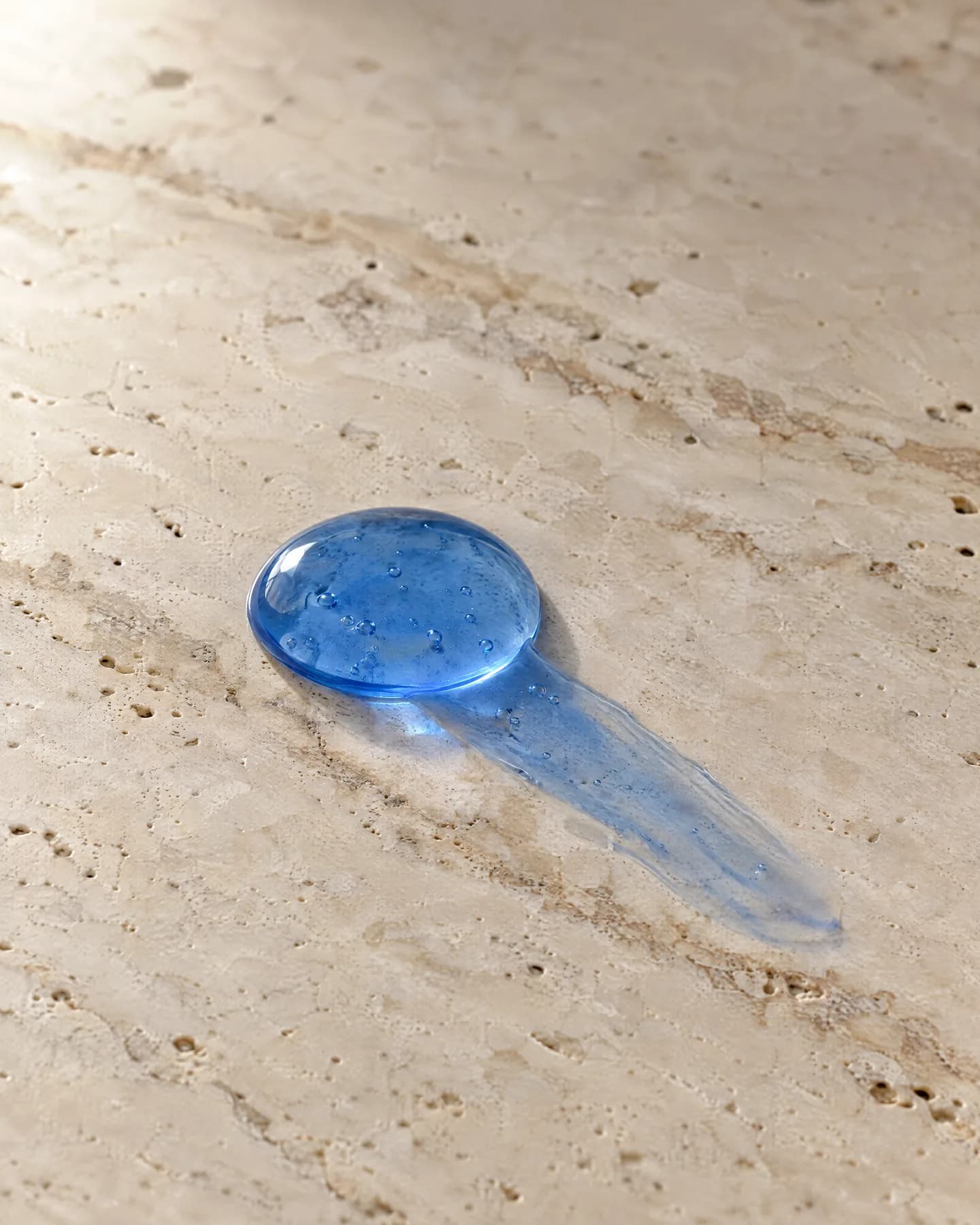 A drop of translucent blue serum on pale travertine.