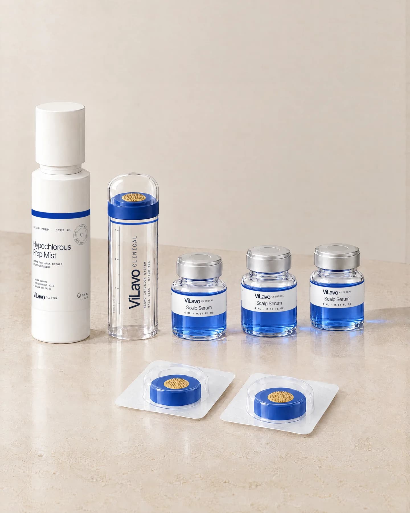 The ViLavo kit on travertine: the Prep Mist, a clear base vial with its dome cap, three small vials of blue serum and two sealed single-use needle heads.