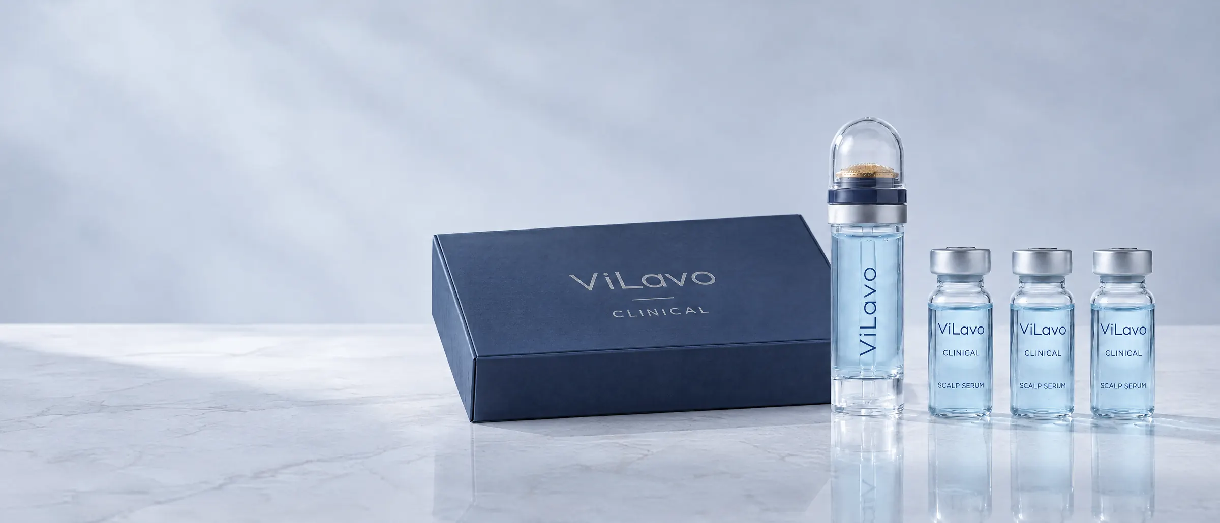 The ViLavo Clinical kit on pale stone: a closed navy box, the micro-infusion applicator and three Scalp Serum vials