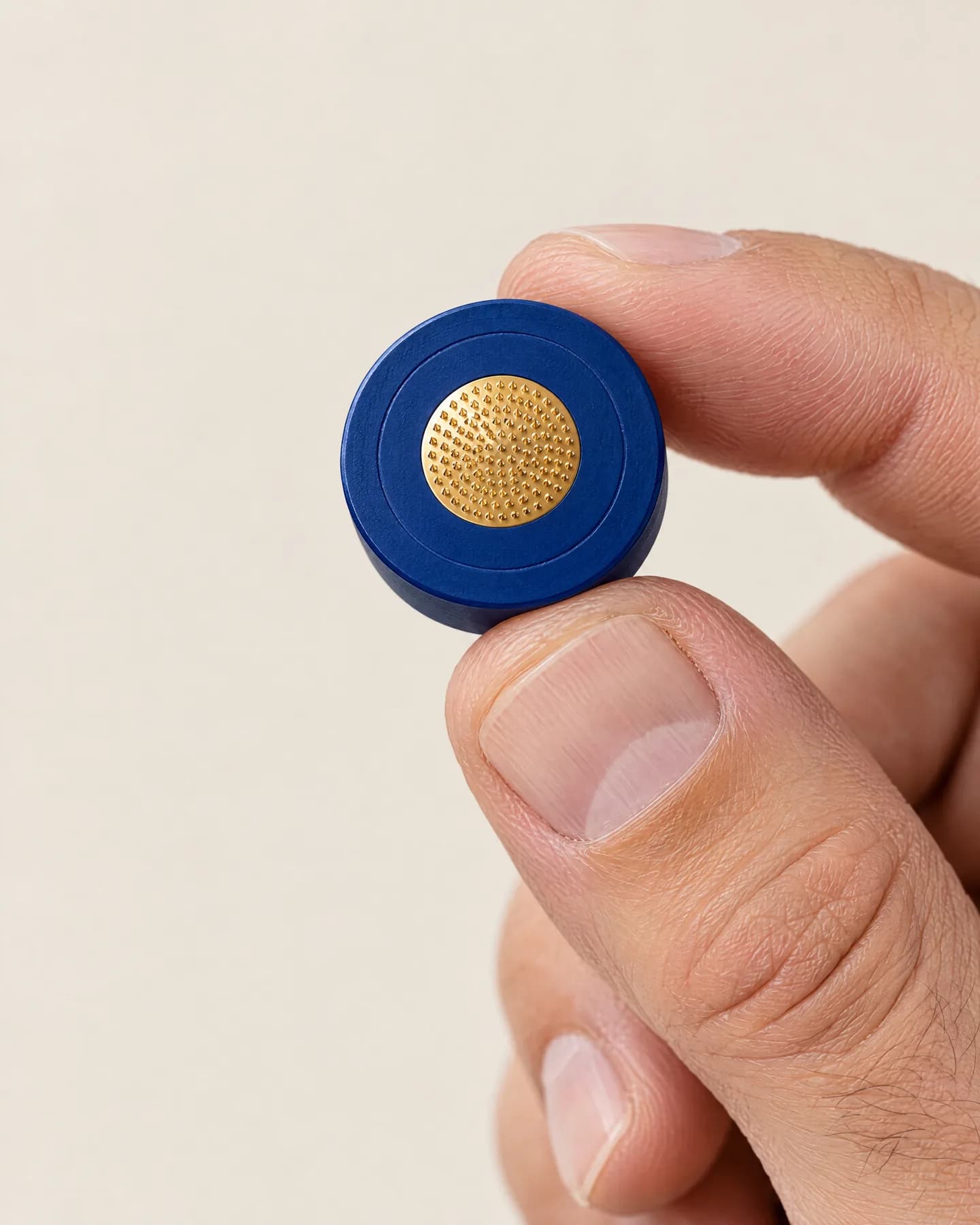A man's fingertips holding a single-use micro-infusion head, its gold micro-needle pad facing the camera.